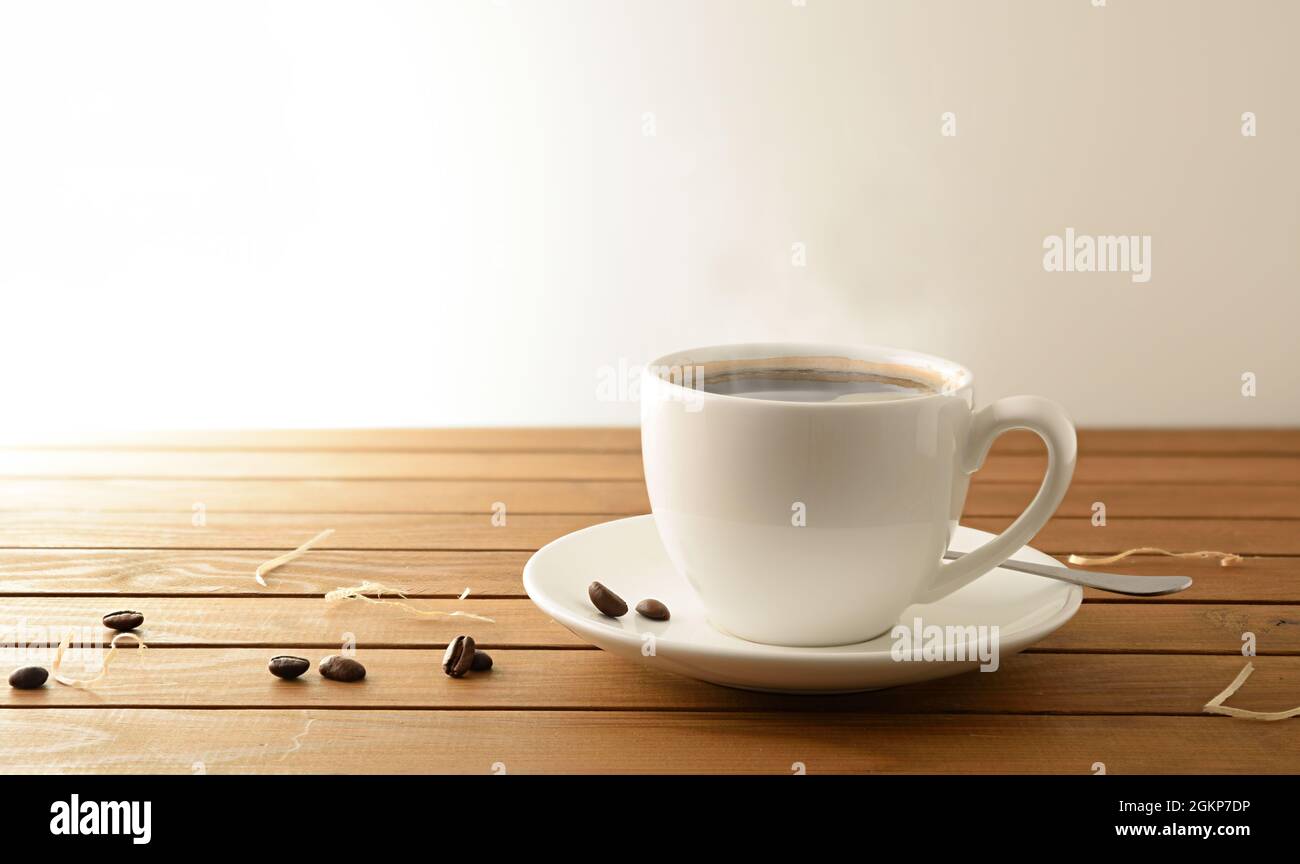 Porzellan weiße Tasse mit heißem Kaffee auf Holzlatten Tisch und Bohnen Detail weiß isoliert Hintergrund. Vorderansicht. Horizontale Zusammensetzung. Stockfoto