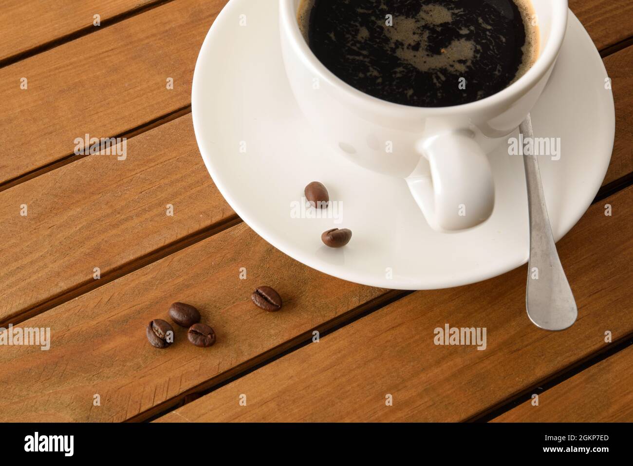Weiße Porzellanbecher mit heißem Kaffee auf Holzlattentisch und Bohnen-Detail. Erhöhte Ansicht. Horizontale Zusammensetzung. Stockfoto