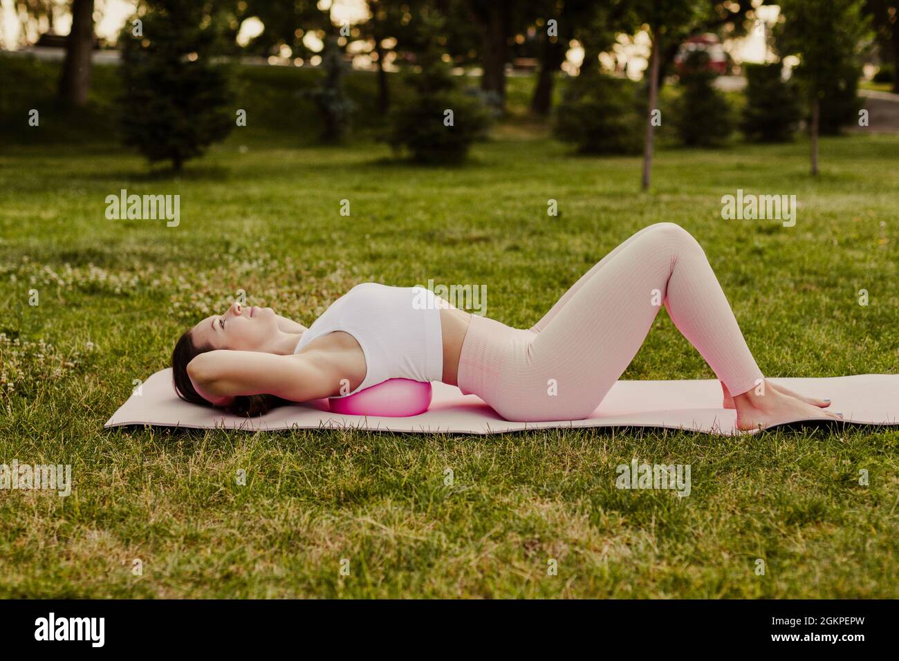 Junge fit Frau in rosa Sportswear liegt mit zurück auf Pilates Ball zu strecken und entspannen Rückenmuskeln im Park im Sommer Stockfoto