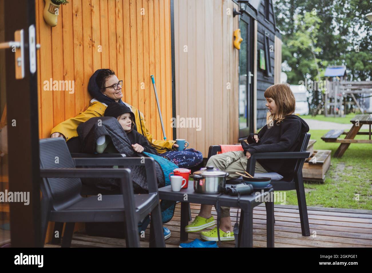 Mutter und Kinder unterhalten sich vor der Holzhütte auf dem Campingplatz Stockfoto