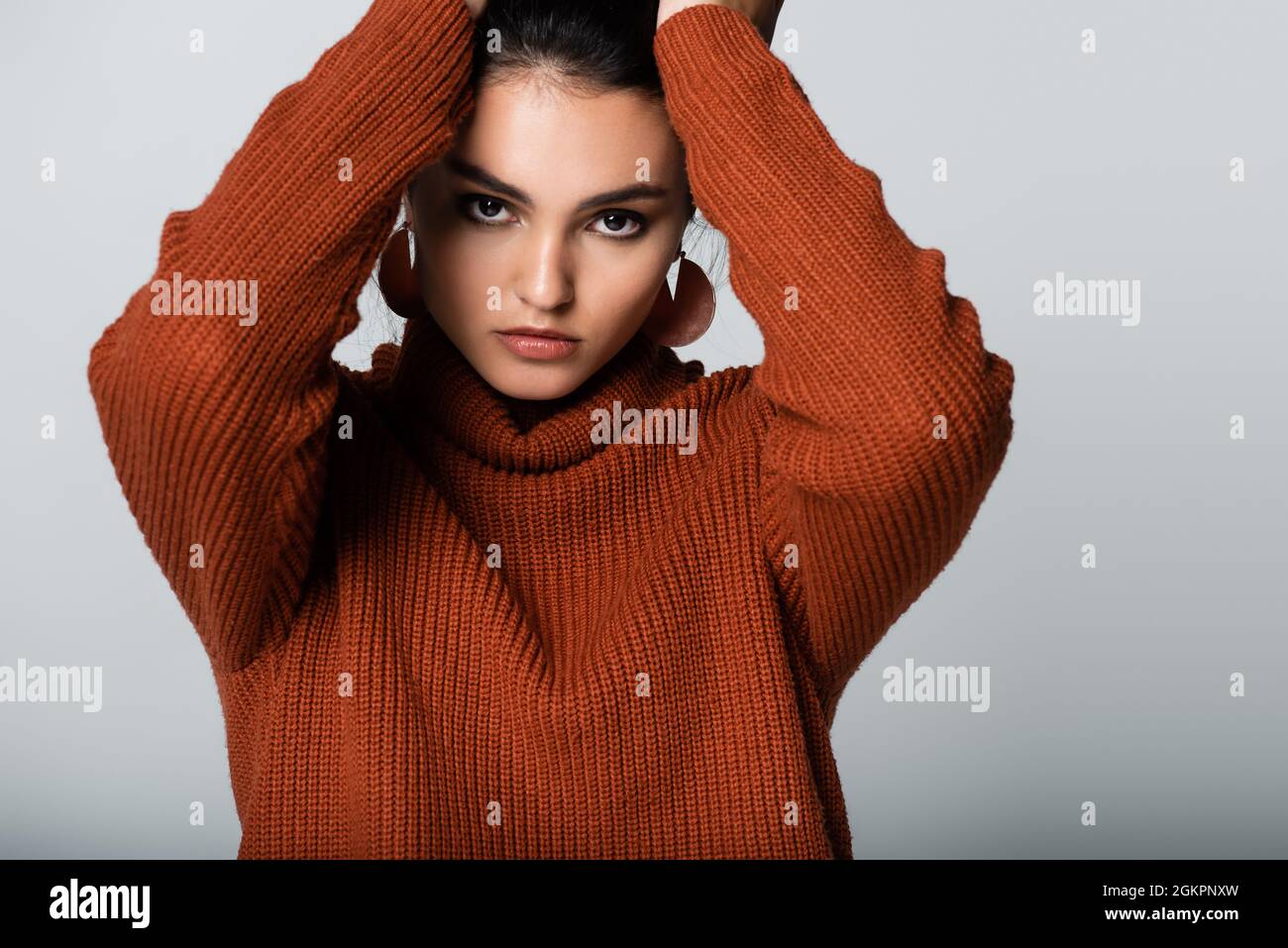 Modell in Ohrringen und Strickpullover mit Blick auf die Kamera isoliert auf grau Stockfoto
