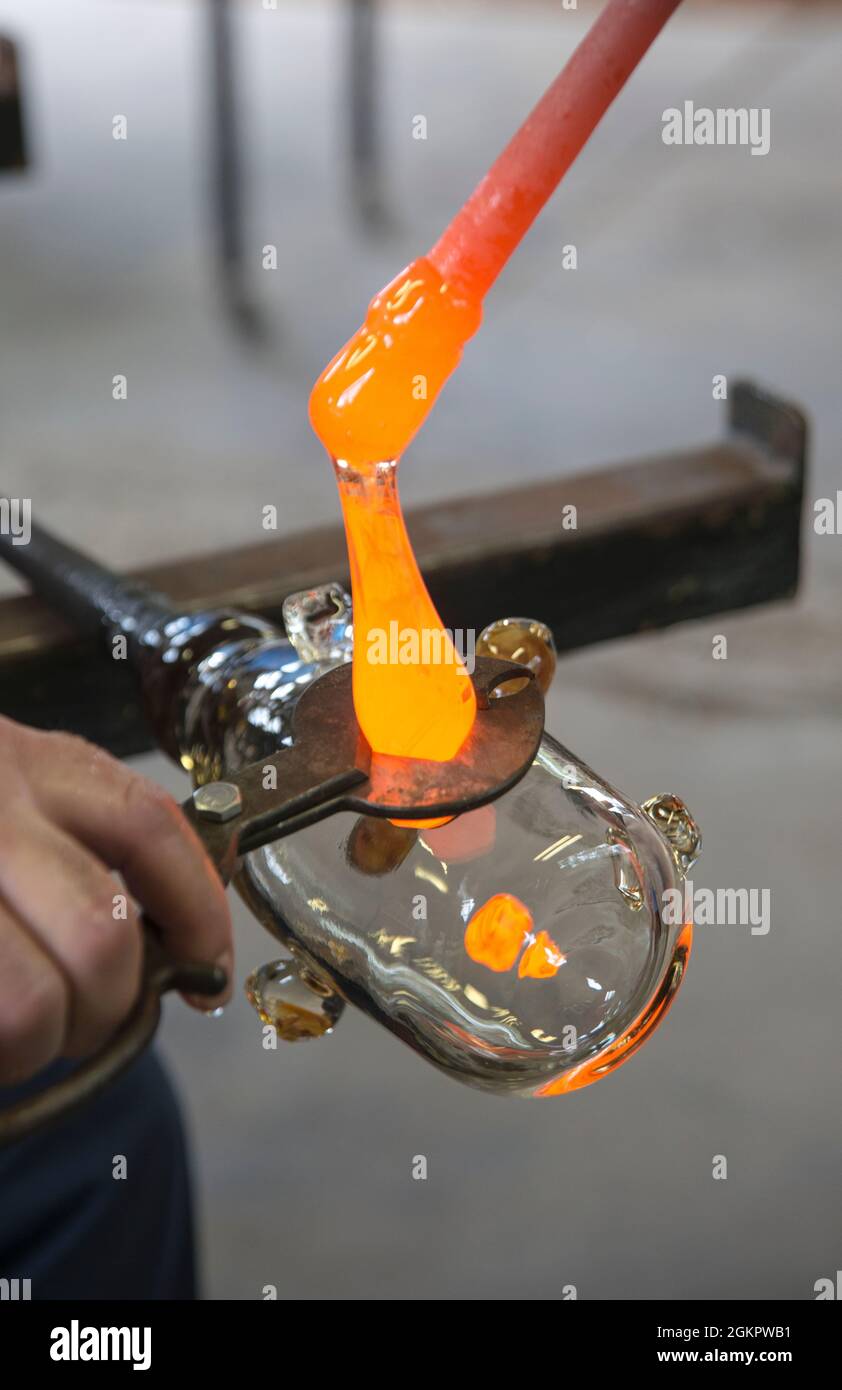 Glasbläser schneidet geschmolzenes Glas mit einem Handwerkzeug Stockfoto