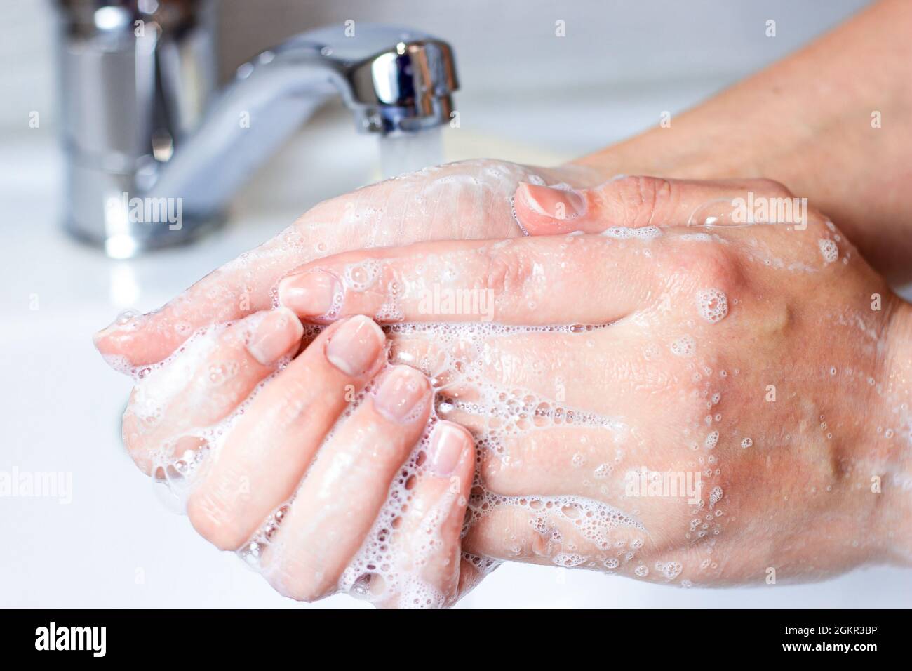 Die junge kaukasische Frau wäscht sich im Badezimmer die Hände mit Wasser und Seifenschaum. Stockfoto