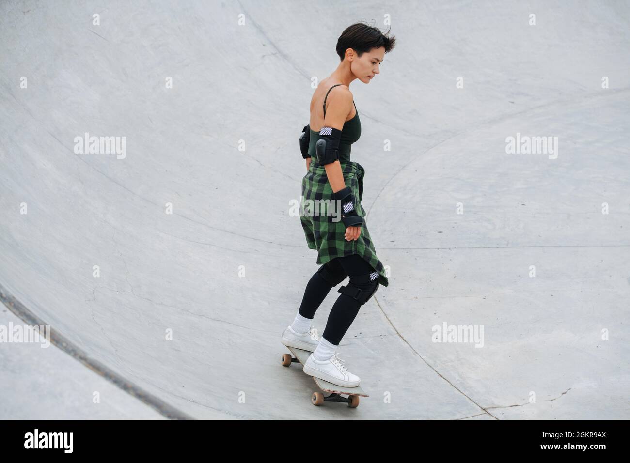 Eingetauchte Skaterin mit kurzen Haaren, die auf ihrem Brett auf einem Viertelrohrkreis reitet Stockfoto Eingetauchte Skaterin mit kurzen Haaren, die auf ihrem Brett auf einem Viertelrohrkreis reitet Stockfoto