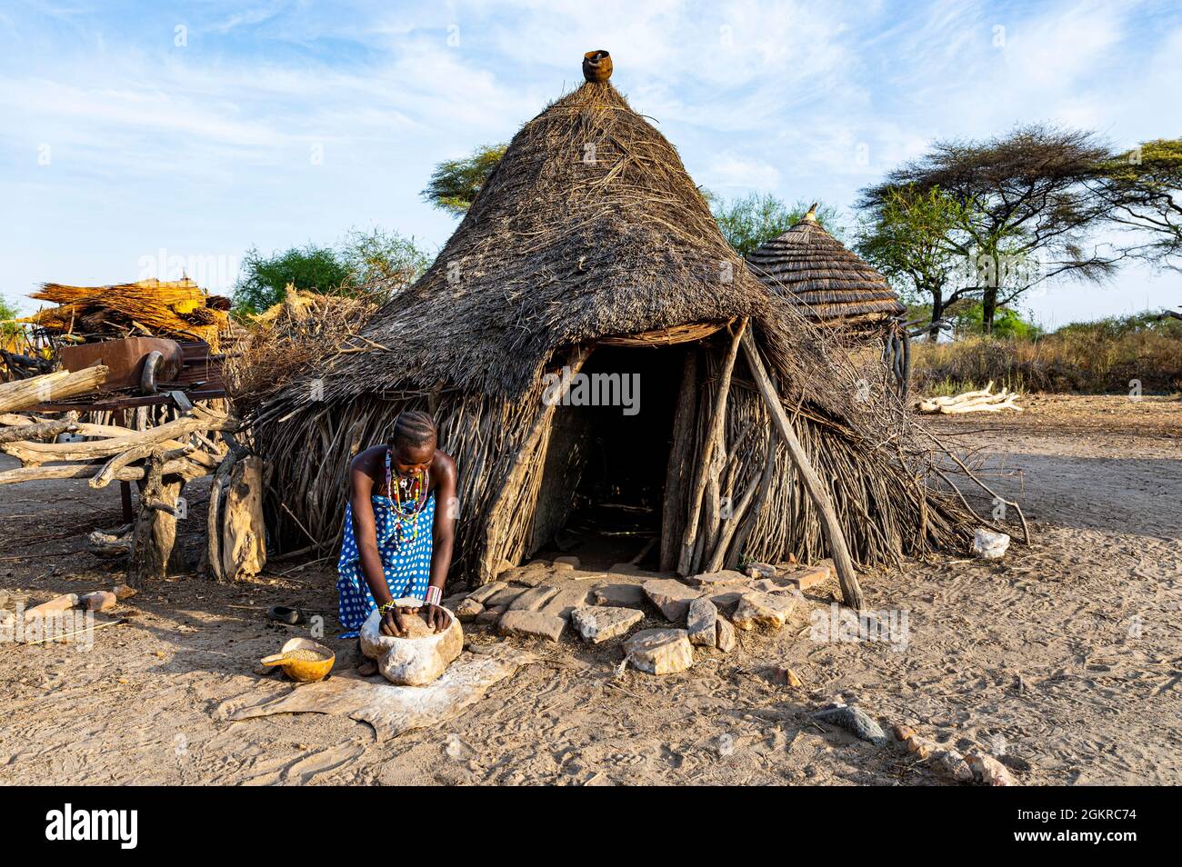 Frau, die Sorghum vor einer traditionellen Hütte des Stammes Toposa, Eastern Equatoria, Südsudan, Afrika, mahlen Stockfoto