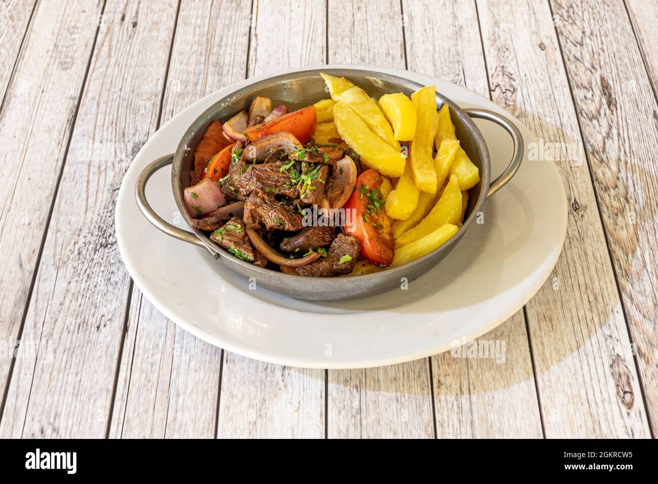 Auflauf aus Metall mit peruanischem Rezept für gebratenes Filet mit Gemüse, Tomaten, Zwiebeln und einer Garnierung aus hausgemachten Chips Stockfoto