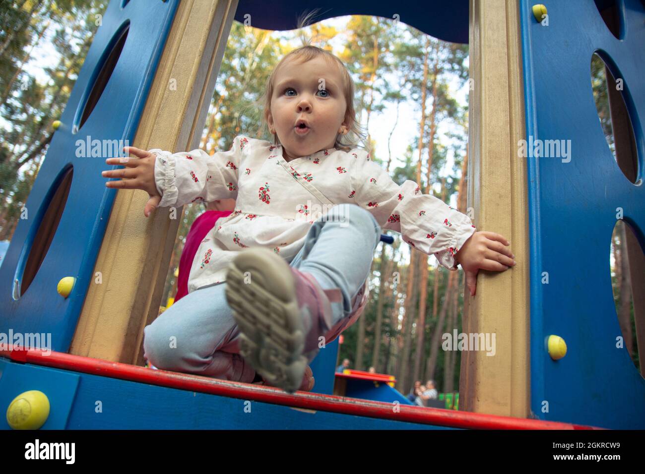Nette liebenswert kaukasischen kleinen Mädchen spielt auf dem Spielplatz im Freien. Ein Mädchen in einem weißen Kleid und ihre Haare in einem Pferdeschwanz. Stockfoto