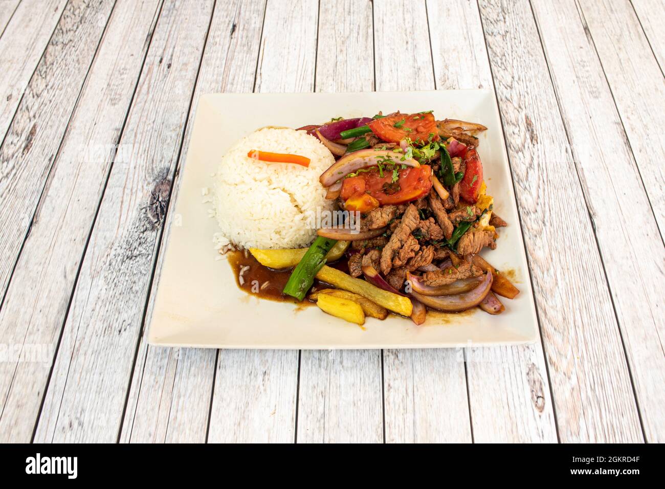 Peruanisches Rezept für Lomo Saltado mit Pommes Frites, weißem Reis, roten und grünen Paprika Twists, Zwiebeln und Petersilie auf einem weißen Teller Stockfoto