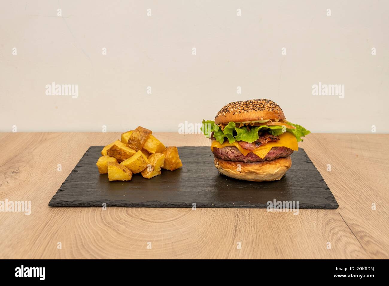 Klassischer Rindfleischburger, doppelt geschmolzener Cheddar-Käse, Zwiebeln und Tomaten, Mayonnaise und Ketchup, geräucherter Speck und Backkartoffeln Stockfoto