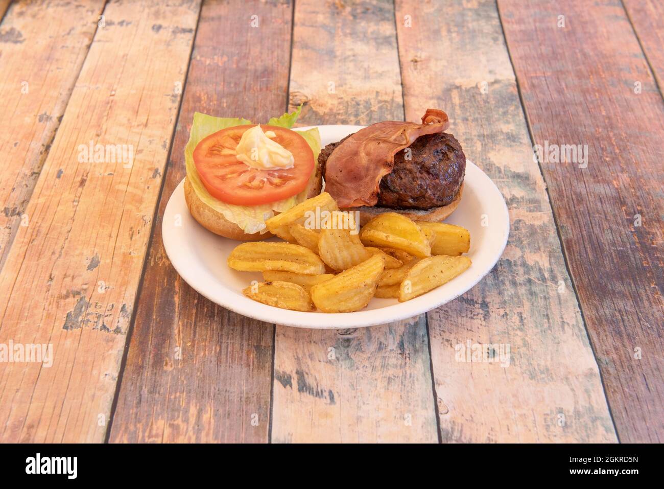 Köstlicher, nicht geschlossener Rinderburger mit geräuchertem Speck, Tomatenscheiben, Mayonnaise und Salat, garniert mit gebratenen Kartoffelkeilen Stockfoto