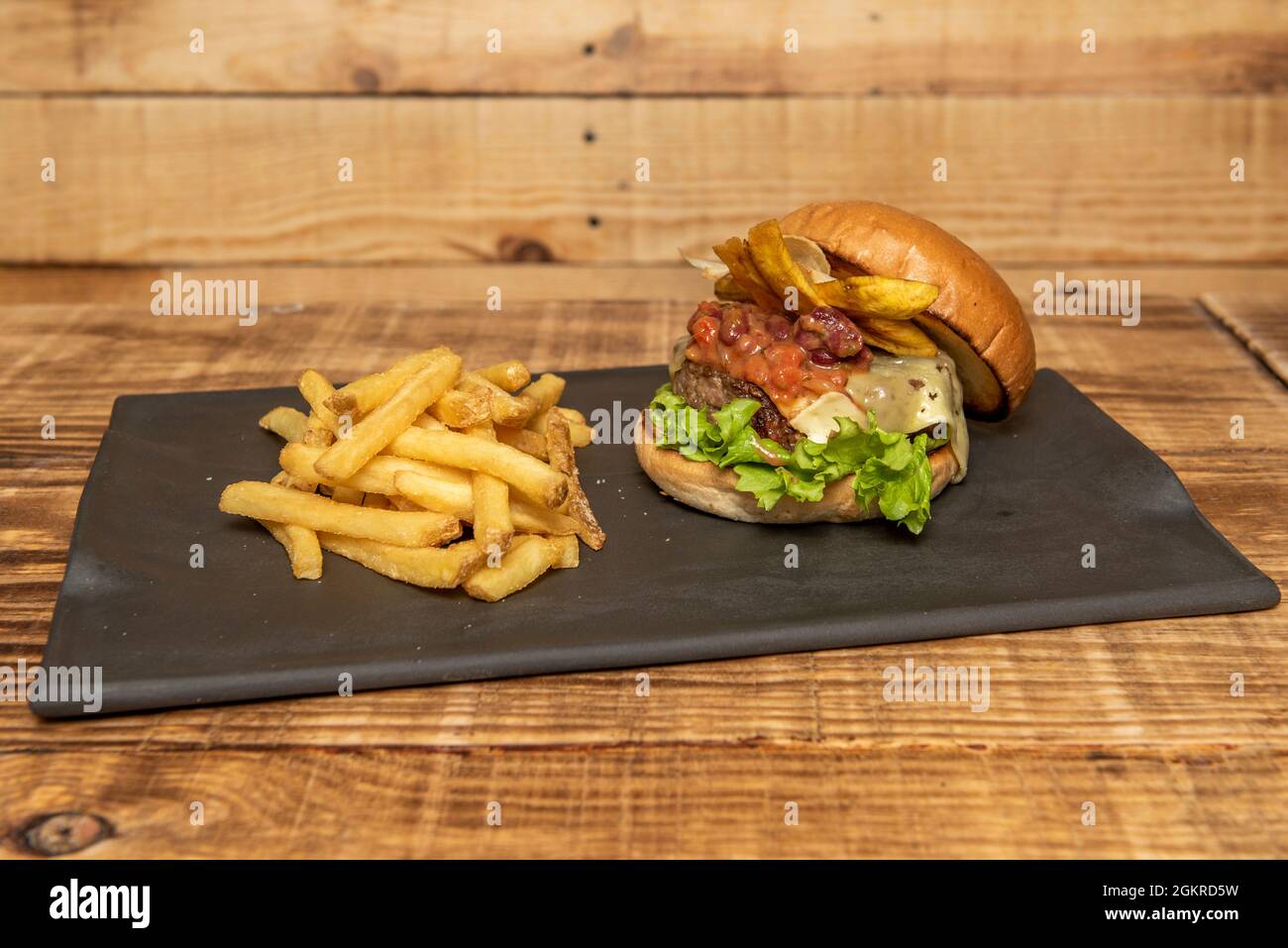 Rindfleisch-Burger nach mexikanischem Stil mit Bananenchips, geschmolzenem Käse, scharfer Bohnen-Chili und Salat mit Pommes Frites Stockfoto