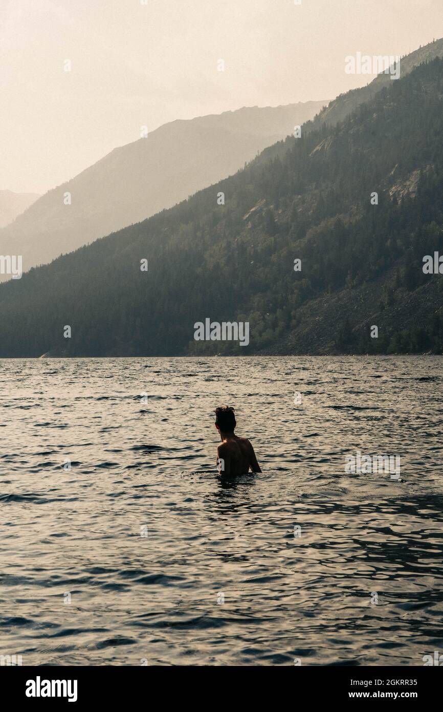 Junger Mann steht am Alpine Mountain Lake bei Sonnenuntergang Stockfoto