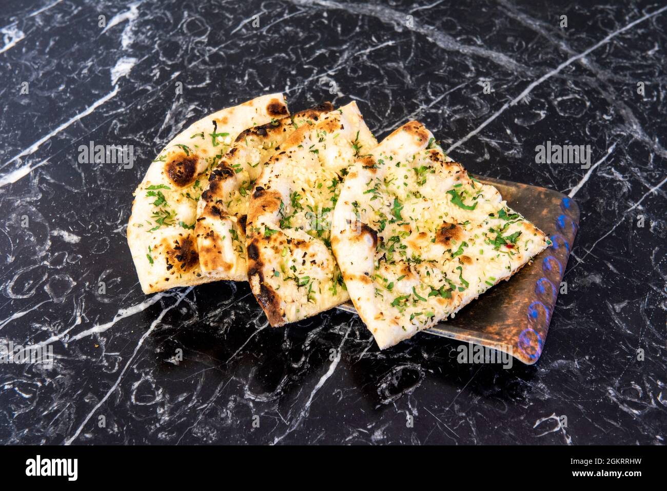 Portionen von Hindu-Naan-Knoblauchbrot mit Petersilie und Nüssen auf dem schwarzen Marmortisch Stockfoto