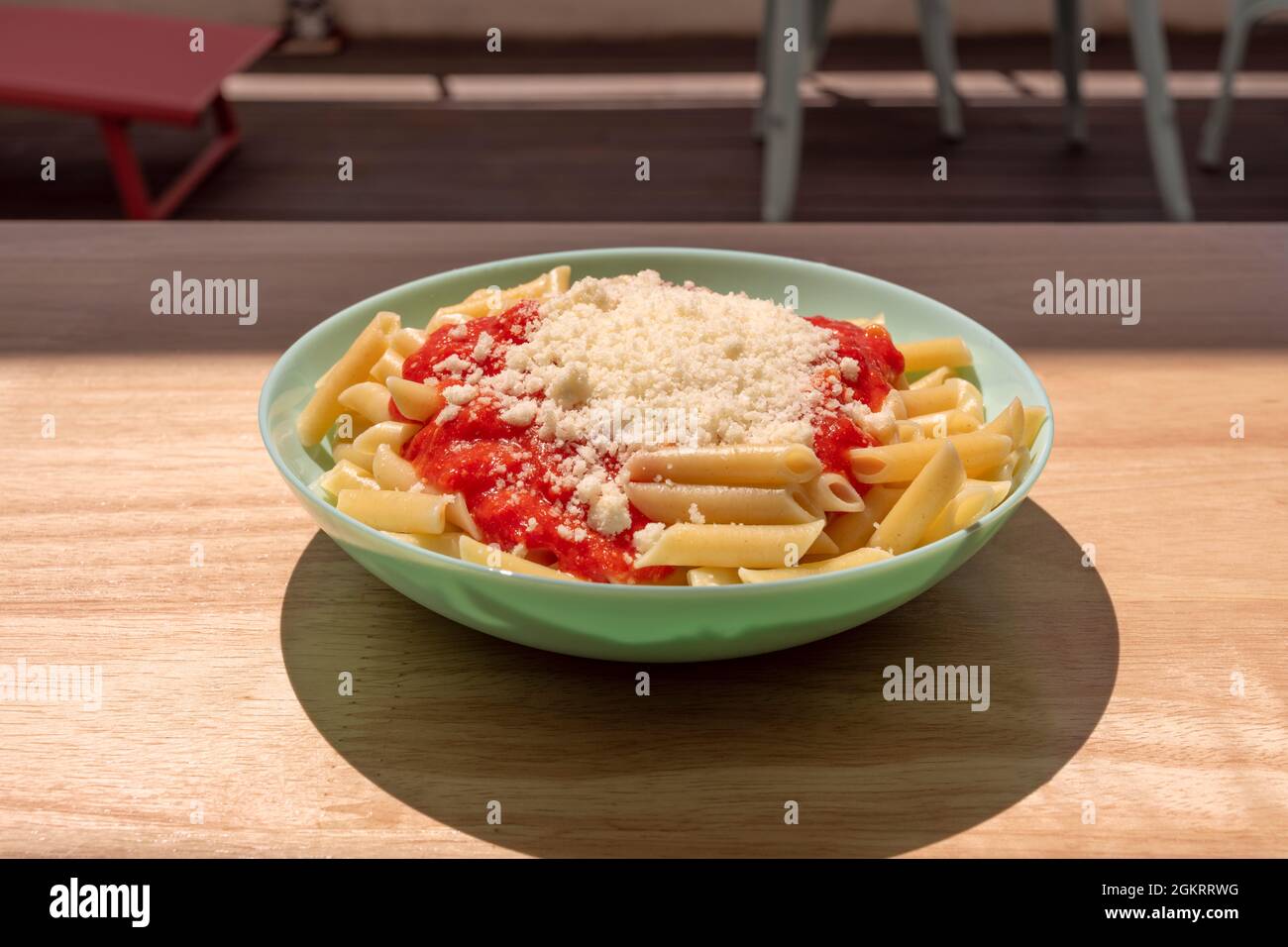 Teller mit italienischen Makkaroni mit Bolognese-Sauce und geriebenem Parmesankäse auf einem hellen Holztisch Stockfoto