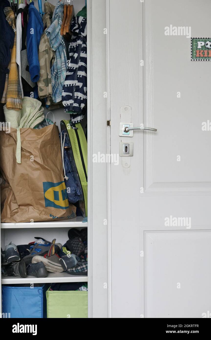 POZNAN, POLEN - 12. Aug 2021: Eine vertikale Aufnahme eines offenen Kleiderschranks mit hängender Kleidung neben einer weißen Holztür Stockfoto