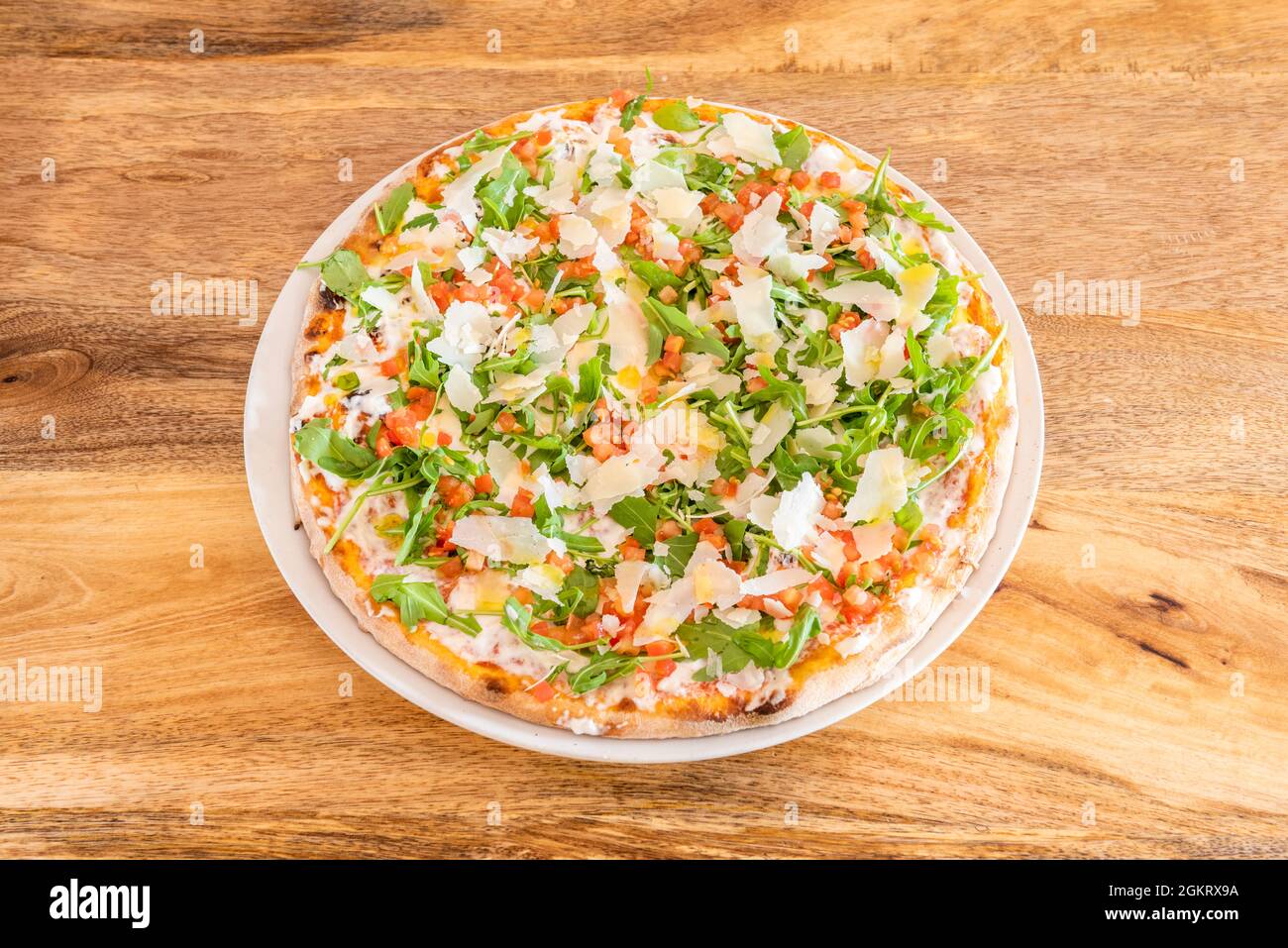 Pizza mit viel Rucola und viel Parmesan in dünnen Krustenflocken und Mozzarella mit gehackter Tomate Stockfoto