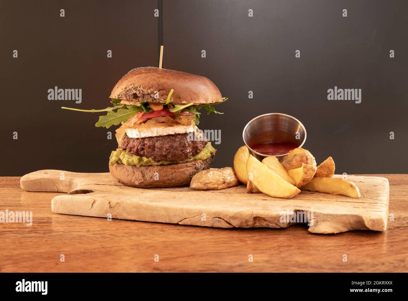 Rindfleisch-Burger im mexikanischen Stil mit Guacamole, Rucola, Ziegenkäse und einer Beilage von Deluxe-Pommes Stockfoto