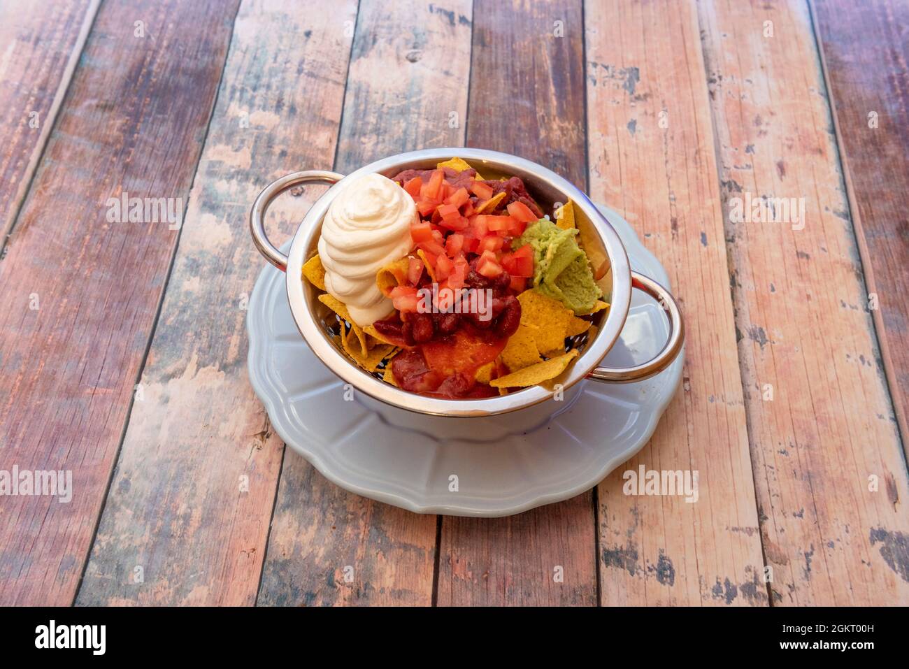 Nachos mit Bohnen, Guacamole und Frischkäse exquisit präsentiert in einer Schüssel mit goldenen Rändern Stockfoto