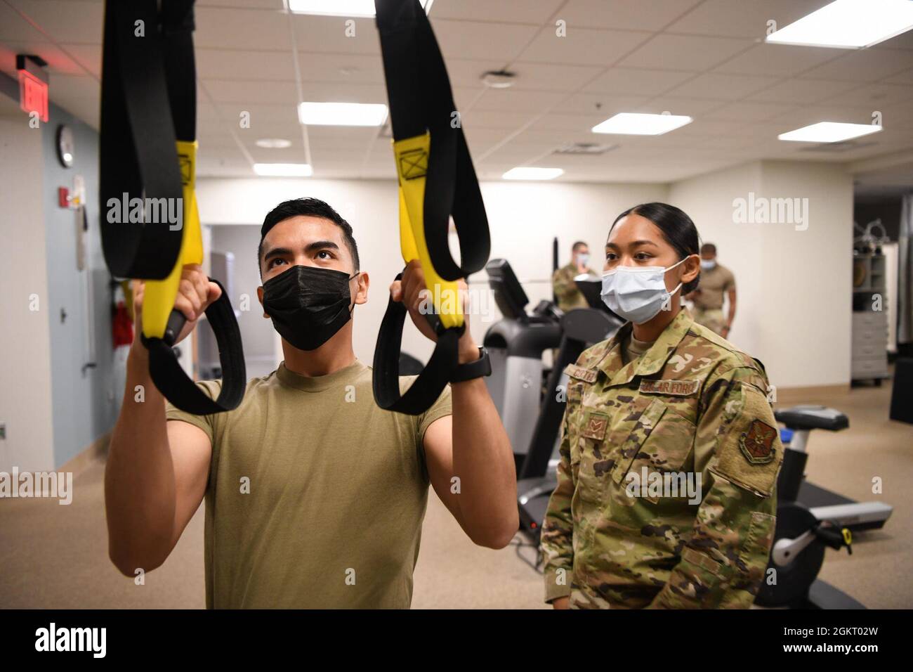 Leitender Airman May Cortez, Physiotherapeut, unterstützt Airman 1st Class Kyle Maglalang, Medizintechniker, während er eine Reihe mit dem Trainingsgerät für Ganzkörperwiderstand durchführt, 24. Juni 2021, in der Medizinischen Klinik bei F.E. Warren Air Force Base, Wyoming. Der TRX wird zur Stärkung und Stabilität des Oberkörpers eingesetzt. Stockfoto