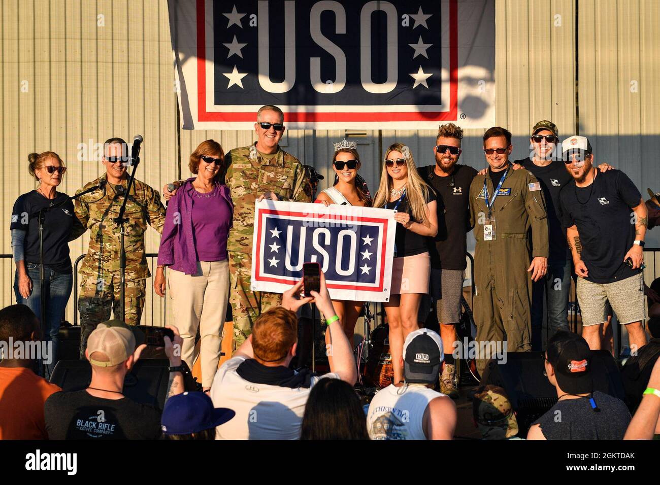 Militärmitglieder und ihre Angehörigen posieren mit USO-Darstellern für ein Gruppenfoto während eines USO-Konzerts auf der Naval Air Station Whidbey Island in Oak Harbor, Washington, 28. Juni 2021. Dies war eines der ersten Live-USO-Konzerte seit Beginn der COVID-19 und NAS Whidbey Island wurde ausgewählt, um ein kostenloses Konzert zu veranstalten. Die USO arbeitet mit renommierten Persönlichkeiten zusammen, um Konzerte, Meet-and-Greets und andere interaktive Veranstaltungen für Service-Mitglieder im in- und Ausland zu veranstalten. Stockfoto