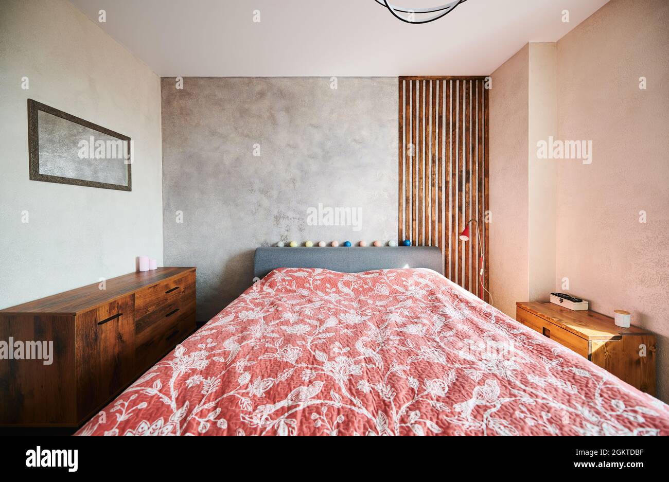 Blick auf das Design des Rutschzimmers mit großem Bett und roter Blumendecke. Schlafzimmer mit zwei hölzernen Kommode. Konzept der Schlafzimmer-Innenausstattung. Stockfoto
