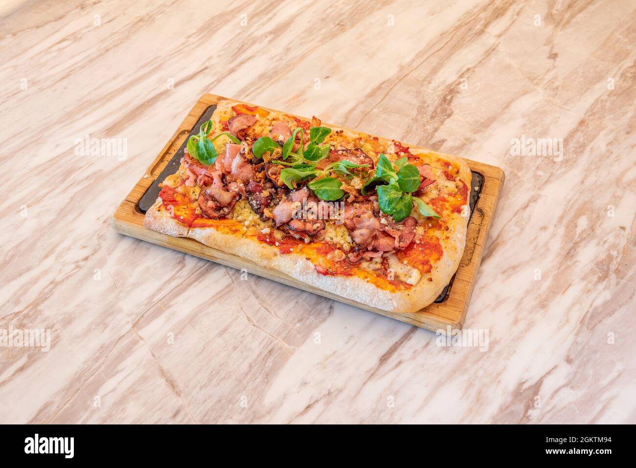 Rechteckige Pizza mit Carbonara-Rezept mit Lammsalat und viel gebratenem Speck, Tomaten und Mozzarella Stockfoto