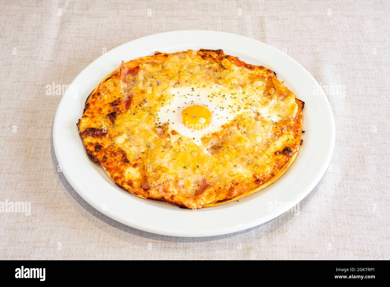 Rustikale italienische Pizza mit viel Käse-Gratin und einem Spiegelei in der Mitte auf einem weißen Teller Stockfoto