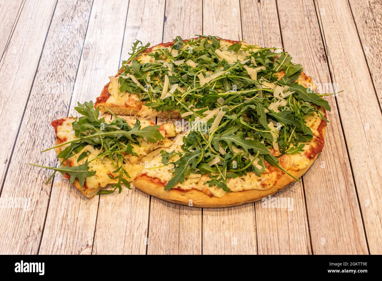 Frische Teigpizza mit viel Mozzarella, Tomaten, viel Rucola und Parmesankäse in Flocken auf einem hellen Tisch Stockfoto