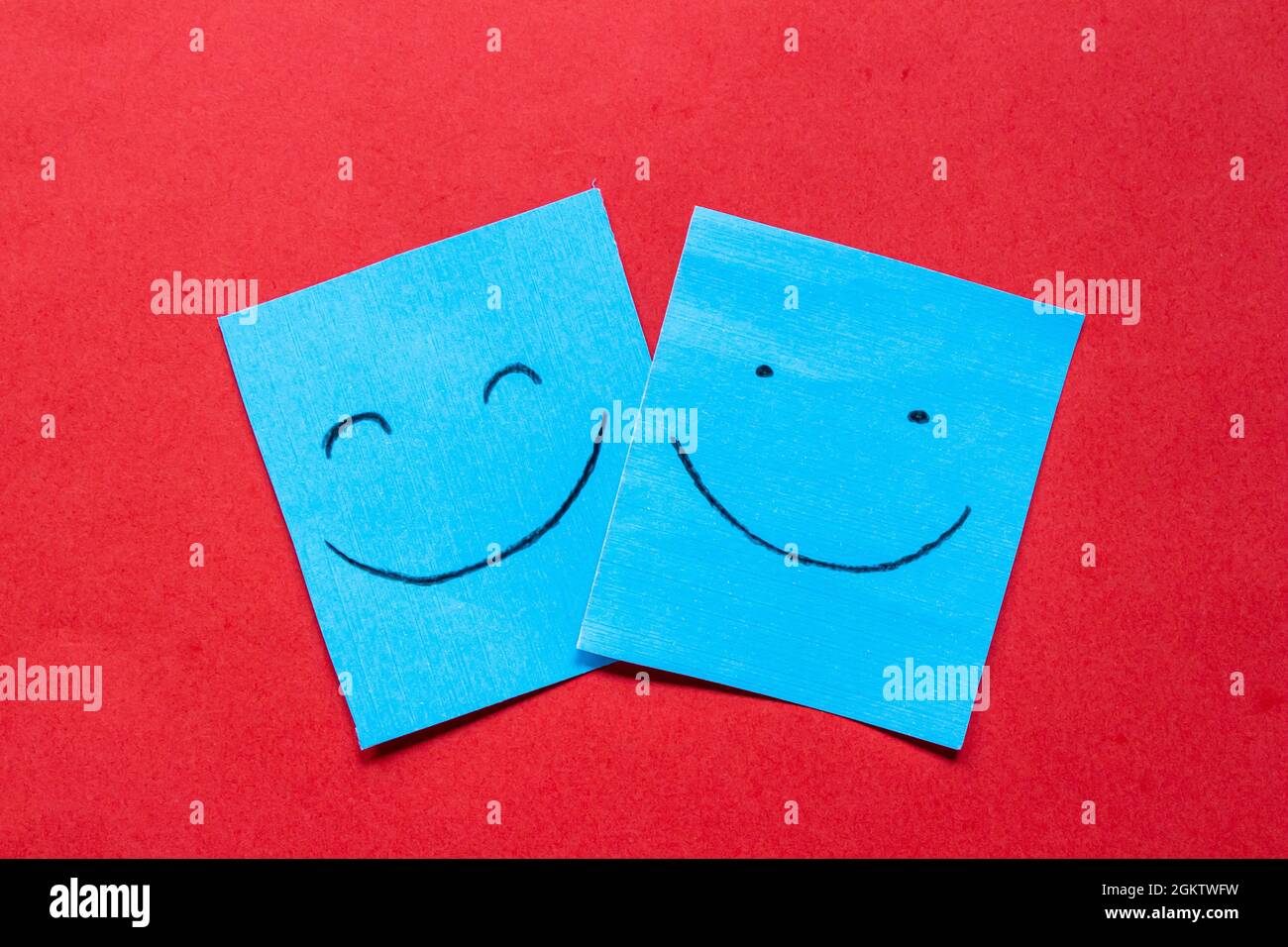 Lächelnde Gesichter auf Papier gezeichnet. Konzept von Glück, Liebe und Freundschaft. Farbaufkleber mit fröhlichem Gesicht auf rotem Hintergrund. Stockfoto