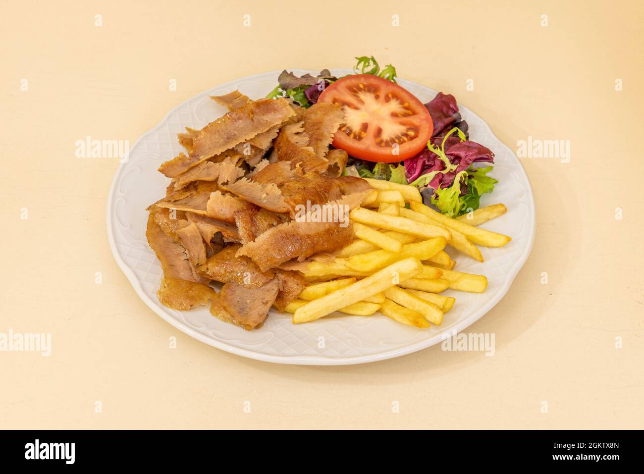 Döner-Teller mit gewürzten Lammscheiben, Bratkartoffeln und Eichensalat sowie Tomatenscheiben in einem Restaurant Döner-Döner auf weißem Teller Stockfoto