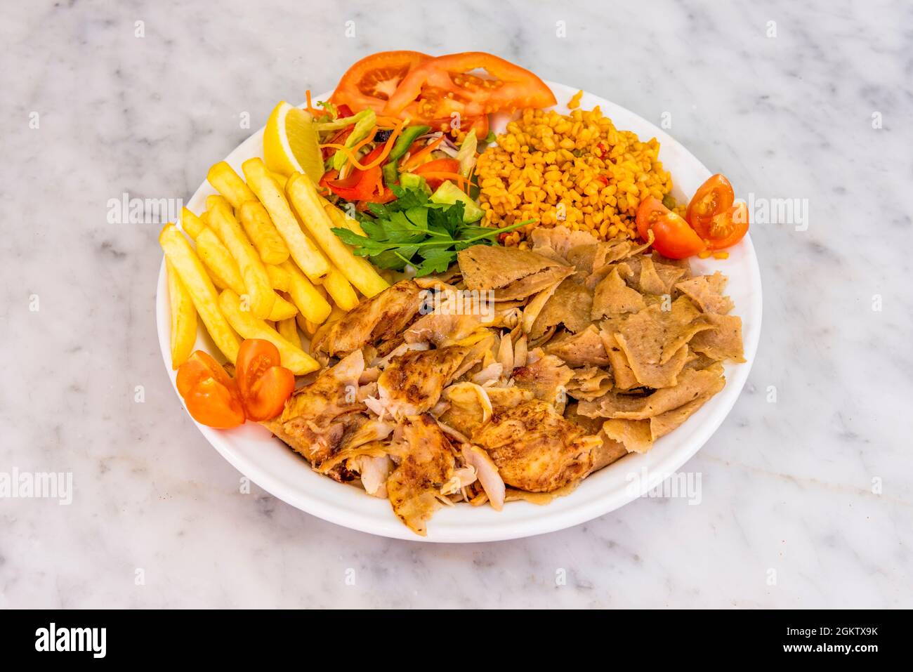 Gemischter Kebab-Teller mit gebratenem Hähnchen- und Lammfleisch, gebratenen Kartoffeln, Bulgur-Eintopf mit Gemüse und Zitrone Stockfoto