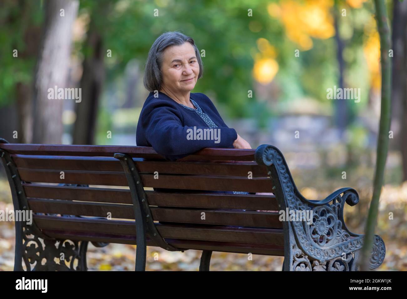 Ältere Frau, die im Herbstpark auf der Bank sitzt und die Kamera anschaut. Stockfoto