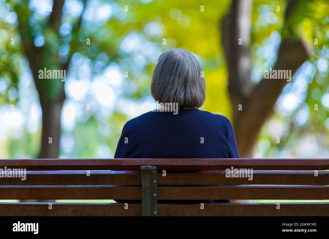 Ältere Frau, die im Herbstpark auf der Bank sitzt. Stockfoto