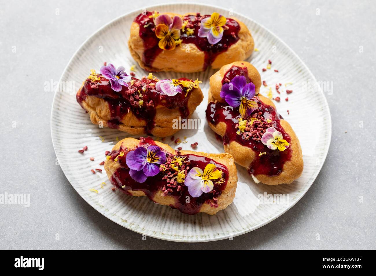 Kleine Eclare mit Blaubeer-Vereisung und violetten Blüten Stockfoto