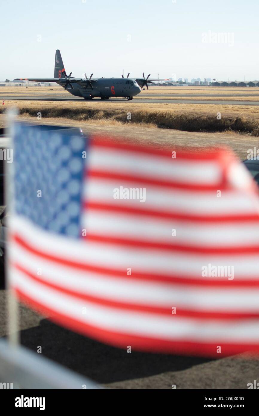 Eine California Air National Guard C-130 nimmt am 14. Juli 2021 an der CAL FIRE Air Tanker Base, McClellan Park, Kalifornien, ein Taxi zur Start- und Landebahn, während die US-Flagge im Wind winkt. Die mit der Air Force C-130 MAFFS ausgerüsteten Flugzeuge von Channel Islands, Kalifornien, wurden vom National Interagency Fire Center angefordert und vom Verteidigungsminister genehmigt und bieten einzigartige Löschkapazitäten. Die MAFFS-Teams der Air Force werden von der 153. Air Expeditionary Group der First Air Force (Air Forces Northern) verwaltet. Stockfoto