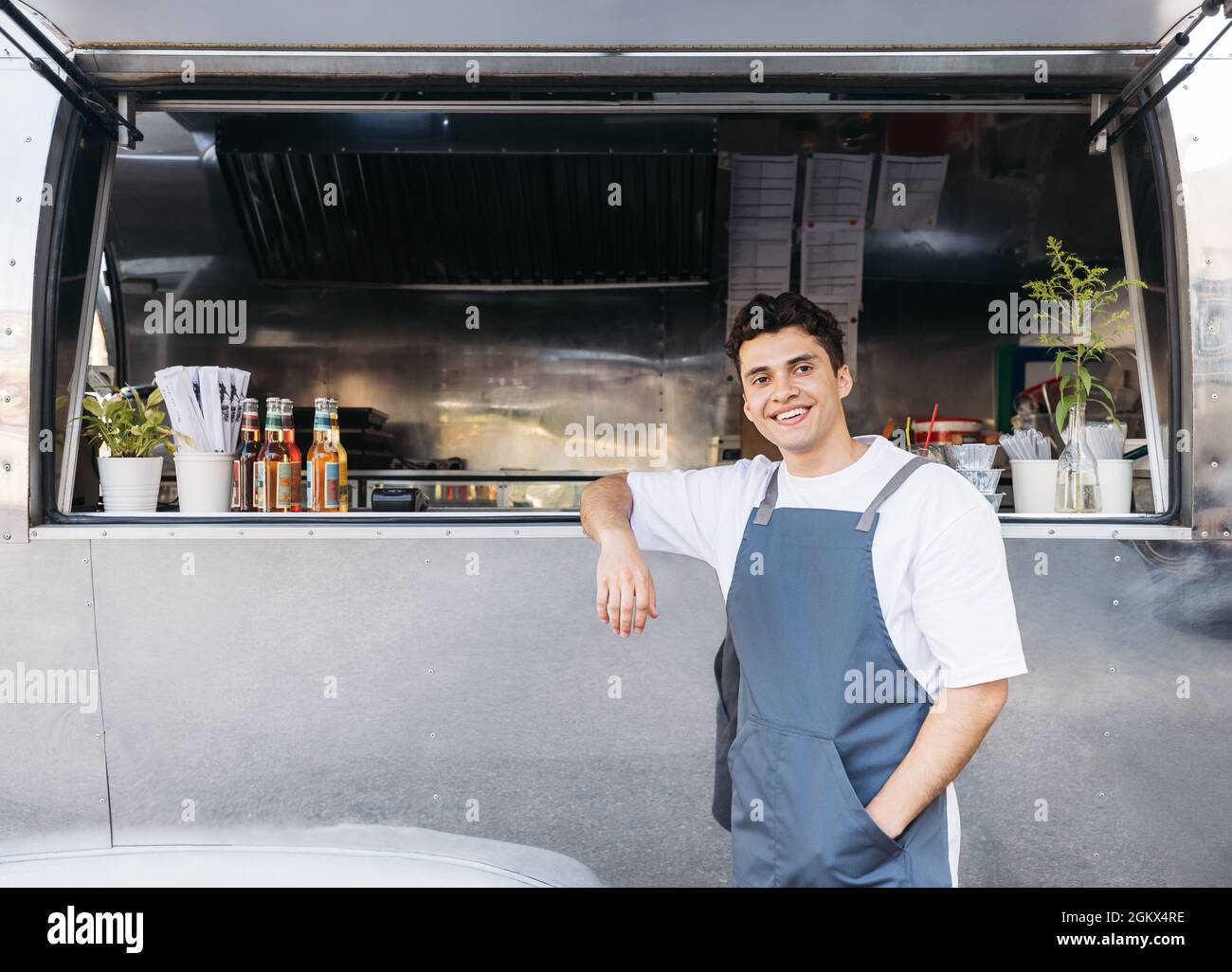 Ein gutaussehender Kellner, der sich auf einen Food Truck stützt. Junger Unternehmer wartet auf Kunden. Stockfoto