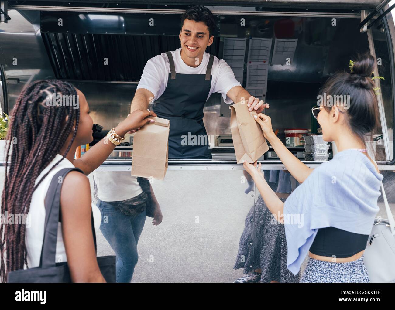Zwei Freundinnen, die verpackte Lebensmittel von einem jungen Unternehmer an einem Food Truck erhalten Stockfoto