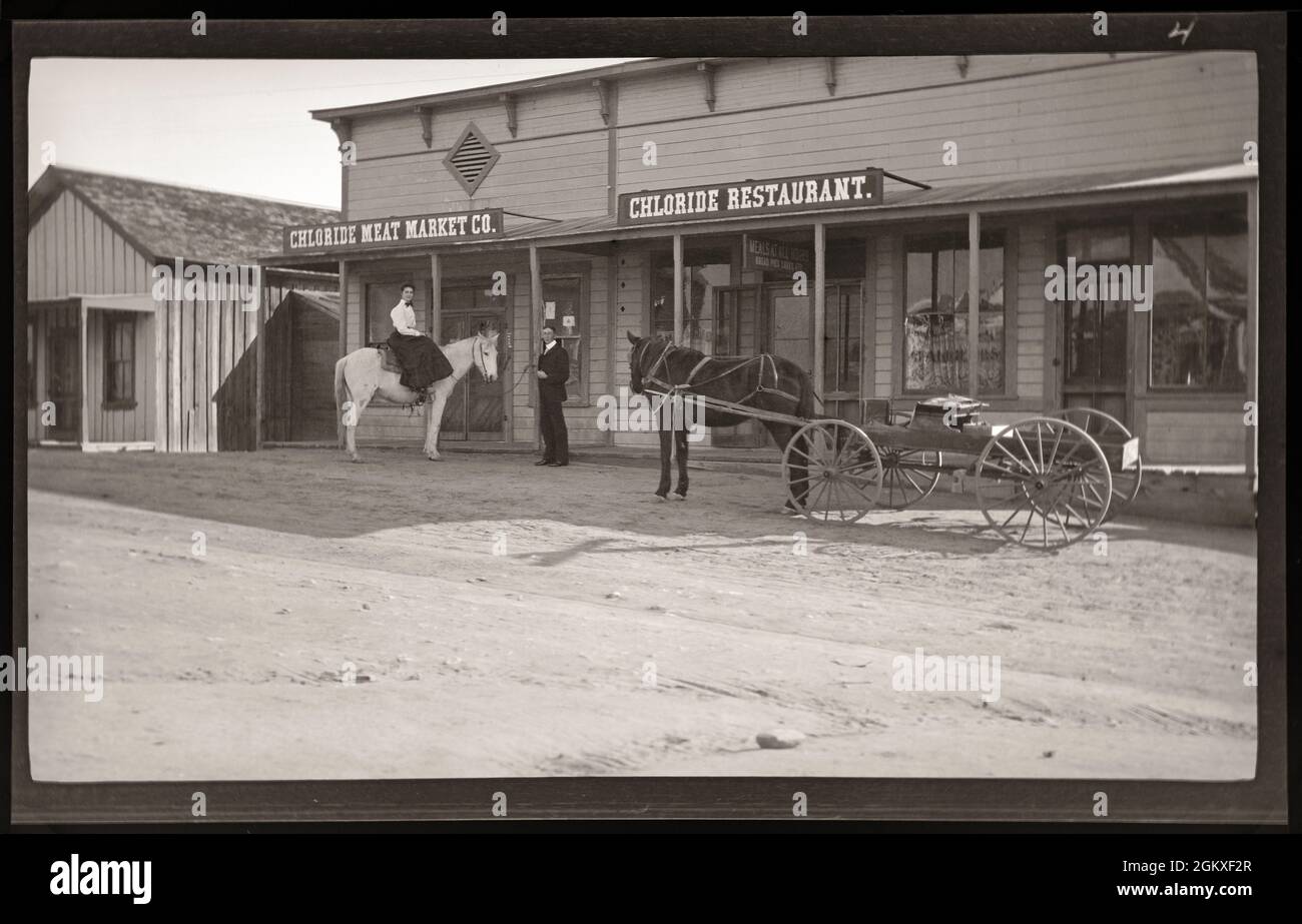 Chloride, Arizona, 1915, eine Frau auf einem weißen Pferd und ein Mann, der neben ihr vor einem Fleischmarkt und Restaurant steht. Inage von 3 x 5 Zoll Nitrat negativ. Stockfoto