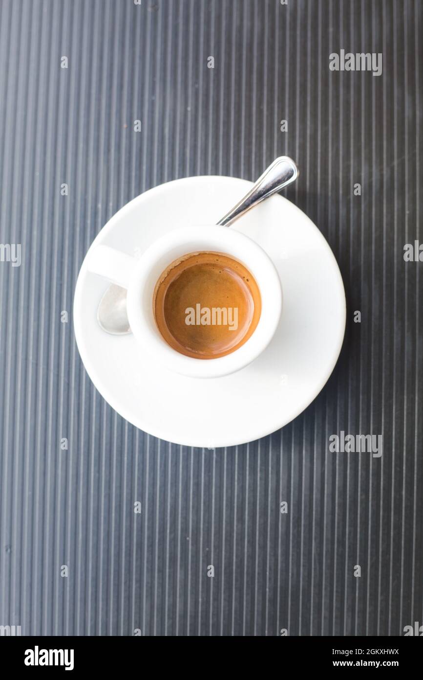 Kaffee mit heißem, frischem Espresso und Teelöffel aus Metall auf grauer Kunststoffoberfläche. Vertikale geometrische Komposition. Blick von oben auf traditionelles italienisch Stockfoto