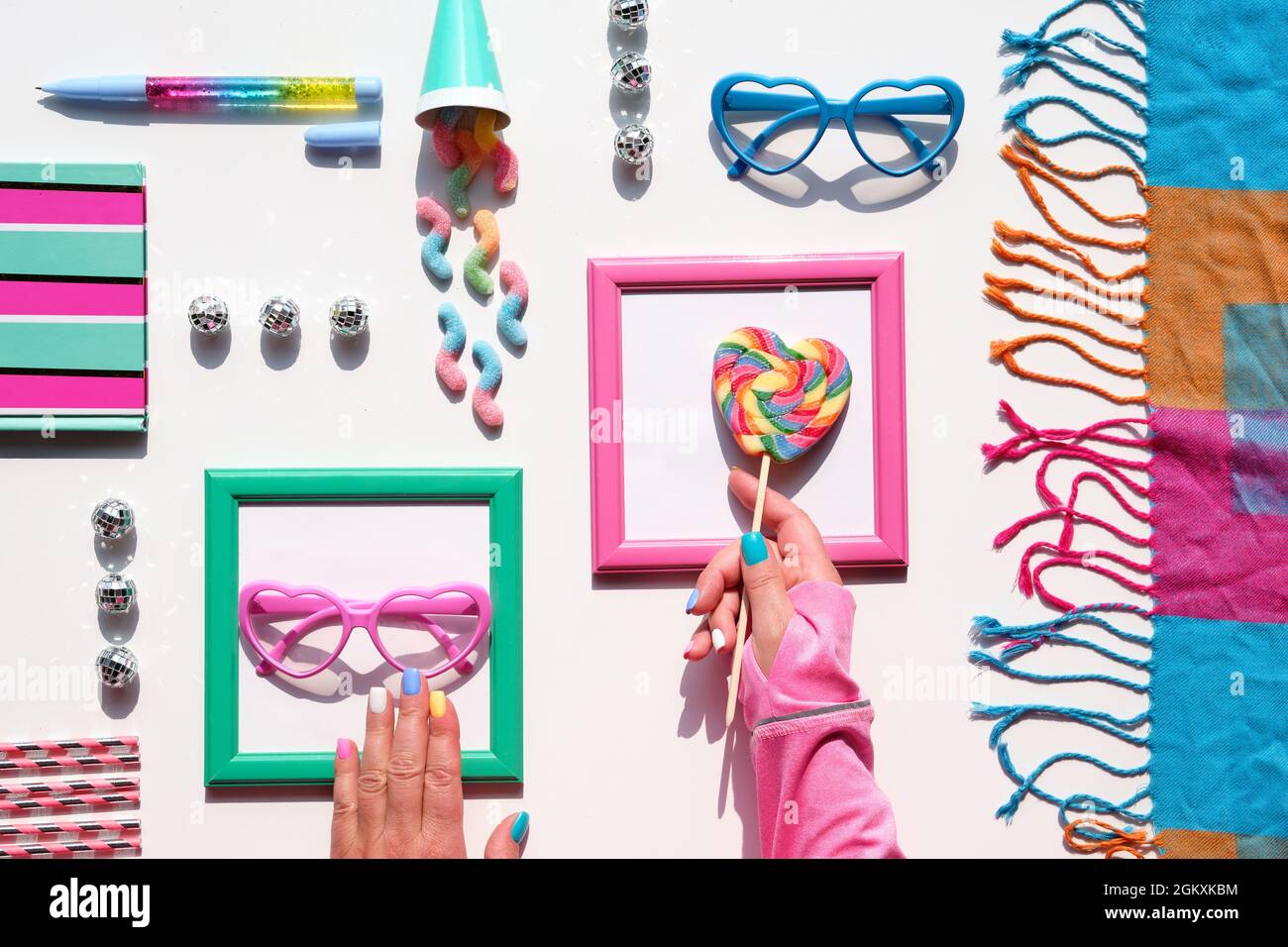 Geburtstag, Urlaub Dekor Hintergrund. Süßigkeiten, Schokolade, Süßigkeiten, süße Snacks. Hand mit Regenbogen-Lollipop-Wirbel. Leckere Snacks und lustige Gläser in Pink Stockfoto