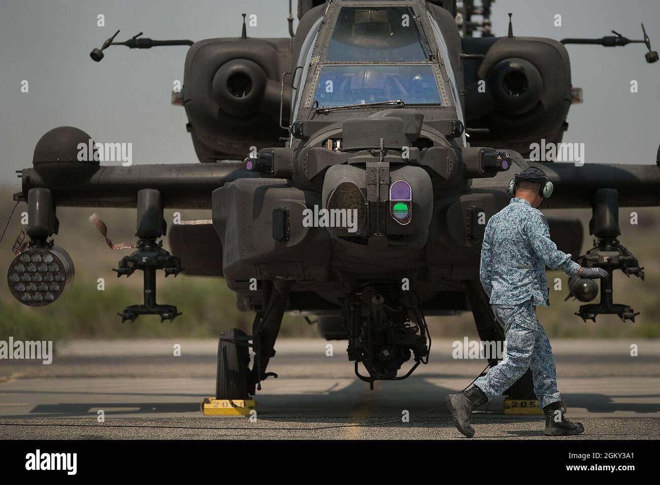 Ein Mitglied der Bodencrew macht sich bereit, die Unterlegkeile zu entfernen, während sich der AH-64 auf das Taxi vorbereitet. Das Orchard Combat Training Center der Idaho Army National Guard war im Juli Schauplatz von Elementen der Luftwaffe der Republik Singapur. Das in Arizona ansässige Kontingent von Singapur betreibt acht AH-64 Apache Helicopters als Teil der Peace Vanguard Task Force. Der Apache ist ein Angriffshubschrauber mit einem Tandem-Cockpit für eine Besatzung von zwei Personen. Es verfügt über einen an der Nase montierten Sensor für Zielerfassung und Nachtsichtgeräte. Es ist mit einem 30 mm M230 Kettengewehr bewaffnet. Es verfügt auch über vier Hardpoints mou Stockfoto