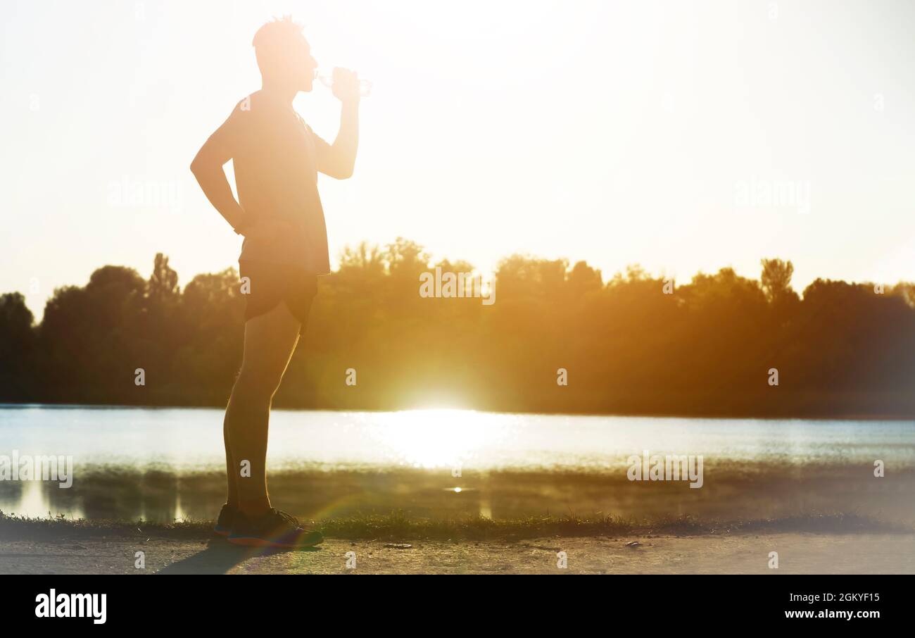 Der Läufer trinkt Wasser, während er im Park joggt. Stockfoto