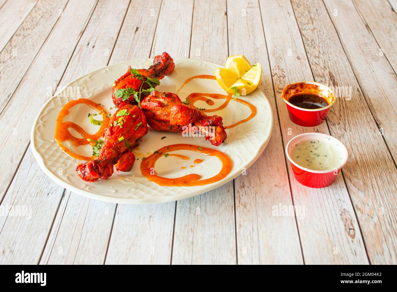 Gebratene Hähnchenschenkel mit asiatischem Tandoori-Huhn gekocht Rezept mit Zitrone, Tomatensauce und Joghurt-Sauce mit frischer gehackter Petersilie Stockfoto