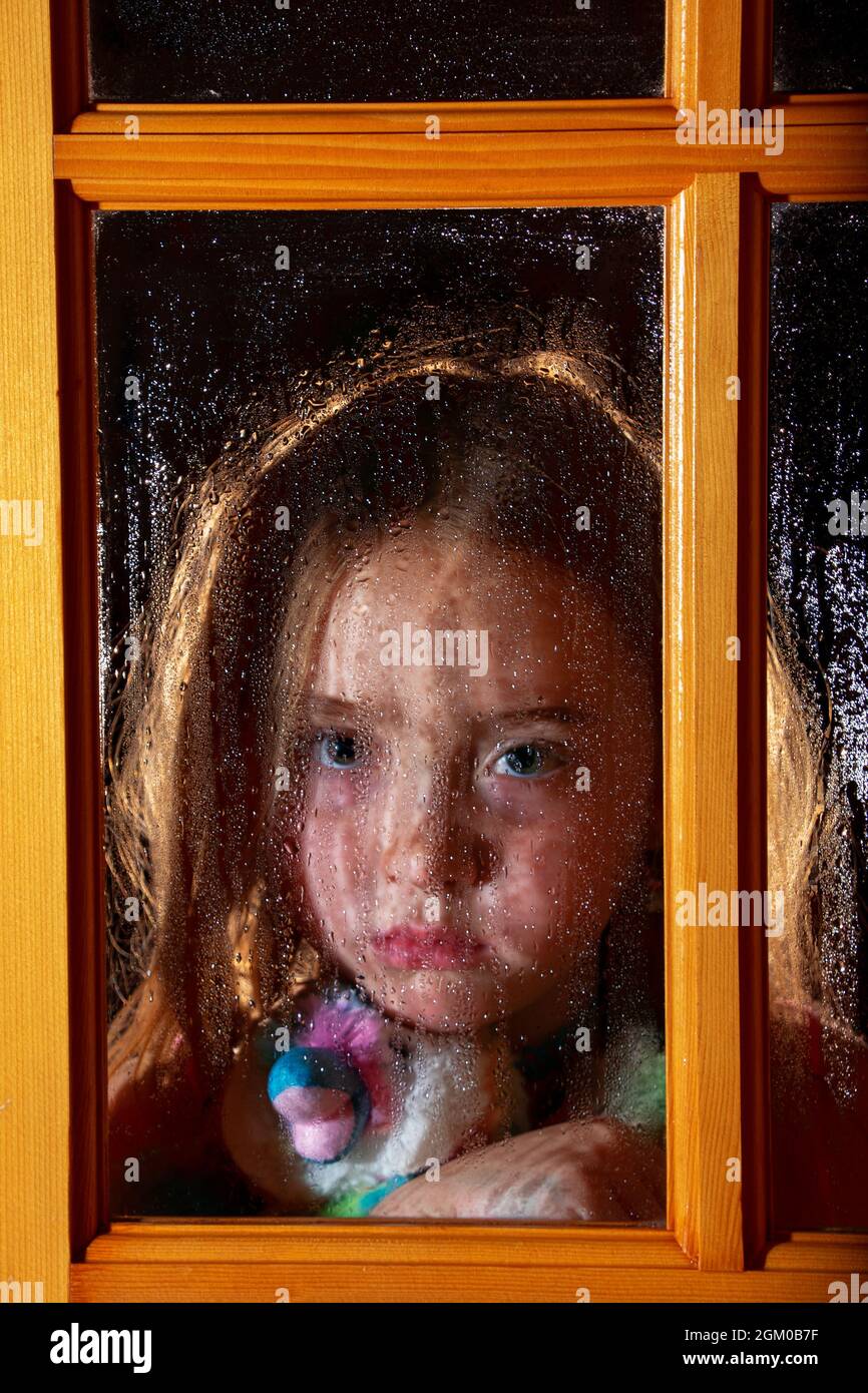 Trauriges Mädchen am Fenster im Regen Stockfoto