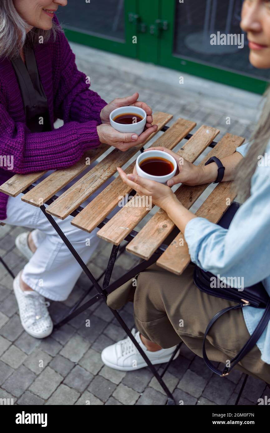 Ältere Damen, alte Freunde, halten Tassen Kaffee an einem kleinen Tisch auf der Terrasse des Cafés Stockfoto