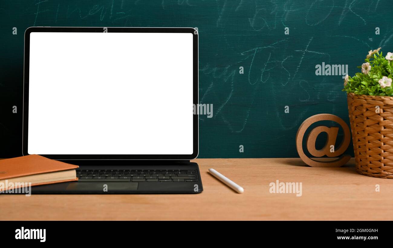 Tablet-Bildschirm-Mockup mit magischem Keyboardständer auf Holztisch mit Dekorationen über grünem Kreidetafel-Hintergrund Stockfoto
