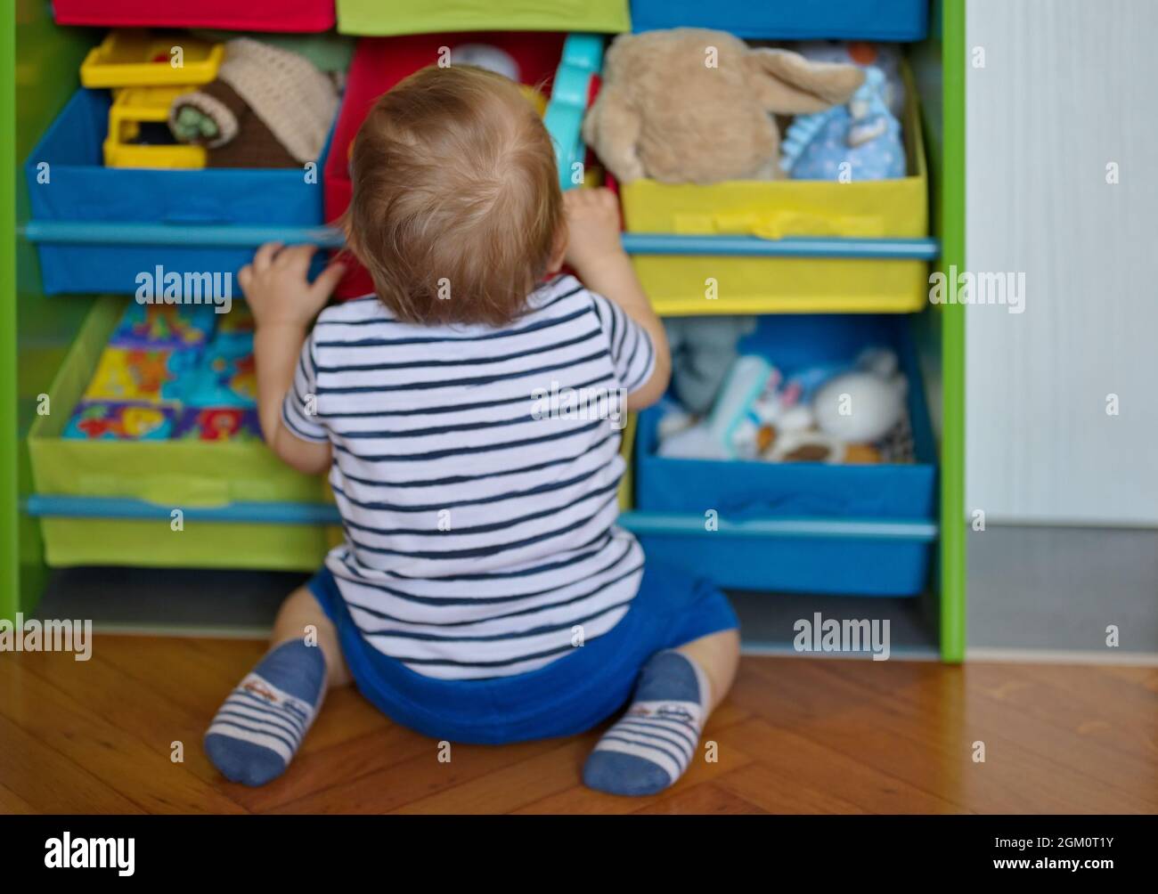 Netter kleiner Junge kniet vor seinem Spielzeugschrank Stockfoto