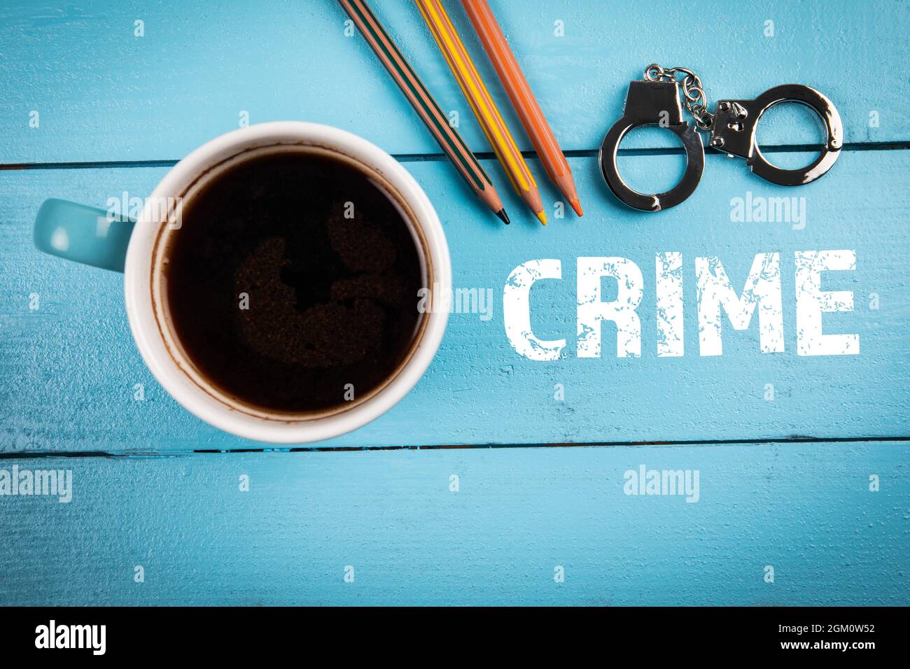 KRIMINALITÄT, Recht, Ermittlungen und Gerichtskonzept. Kaffeebecher und Miniaturhandschellen auf einem Holztisch. Stockfoto