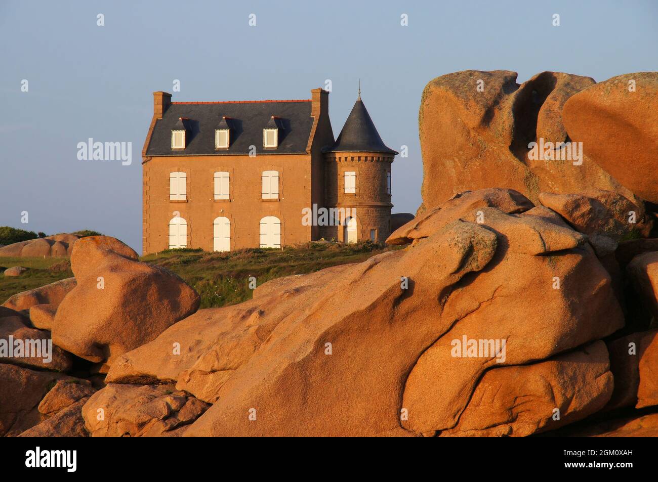 Lebhaft rote Granitfelsen und Haus kurz vor Sonnenuntergang in der Nähe von Phare de Men Ruz und Ploumanac’h, Cotes d’Armor, Frankreich Stockfoto