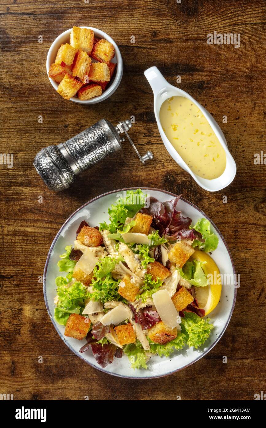 Klassischer Caesar-Salat, oberer, flacher Lay Shot mit klassischer Sauce auf Mayonnaise-Basis, Croutons und Pfeffer auf dunklem, rustikalem Holzhintergrund Stockfoto